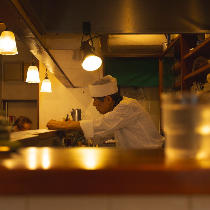 夕方の厨房。灯りの下で仕込みをする料理人
