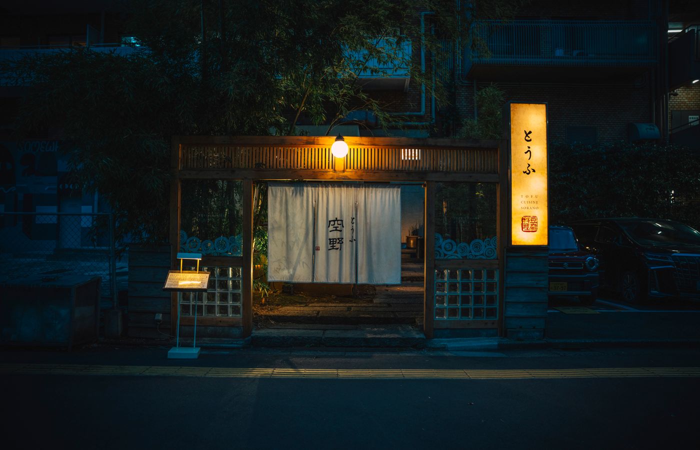 夜、灯りのついた店の入り口。小さな看板と暖簾