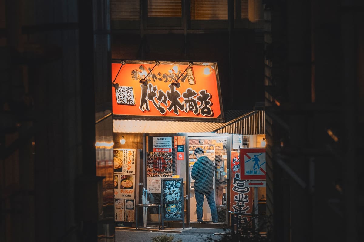 暗い路地に、橙色の看板と窓の明かりが灯る小さな店