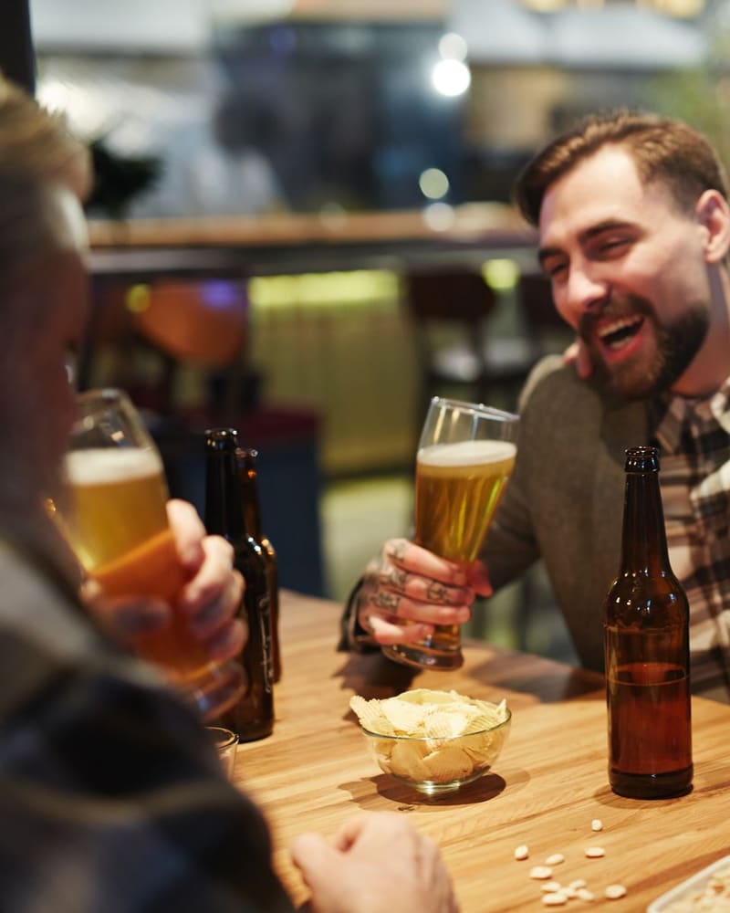 木のテーブルで、ビールを手に笑い合う2人