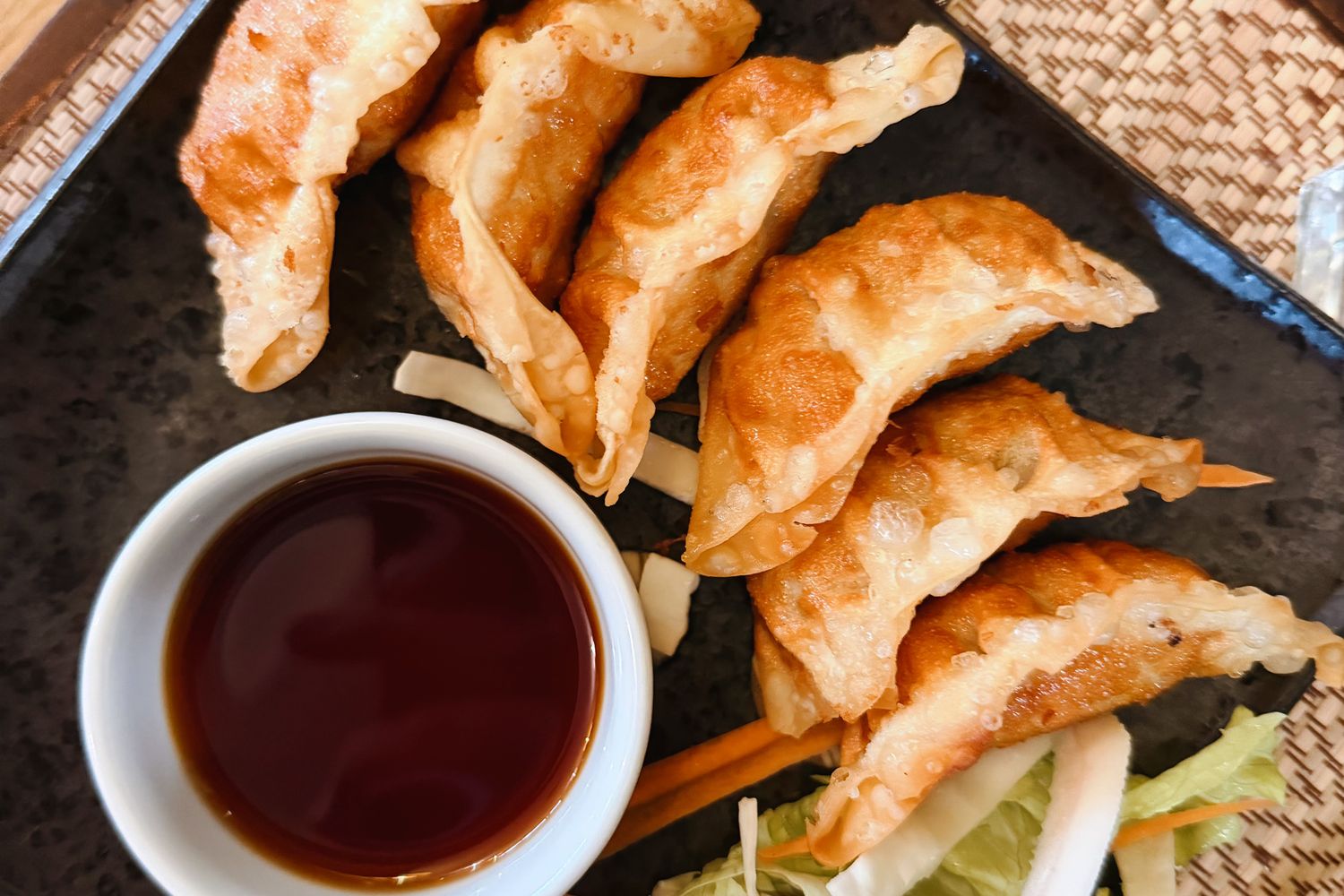 黒いトレーに盛った、揚げたての手包み焼き餃子とつけダレ